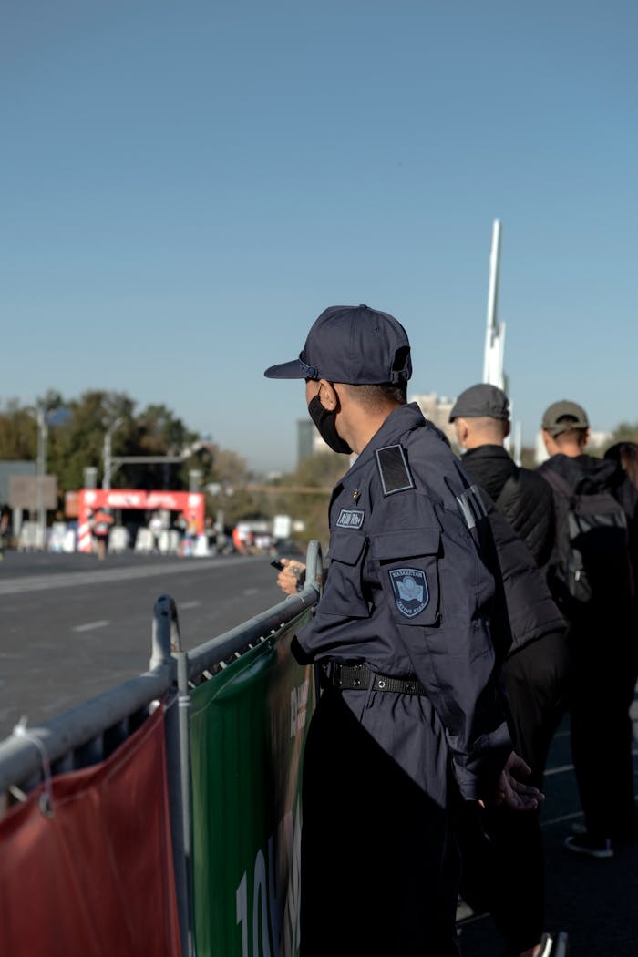Police officer in uniform observing a public event by the roadside in daylight.